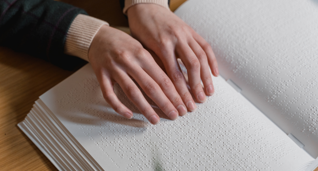 deux mains lisent une page d'un livre en braille ouvert.