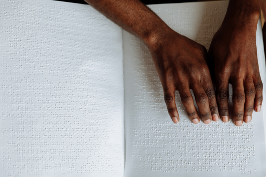Deux mains à la peau foncée lisent le braille sur une page.