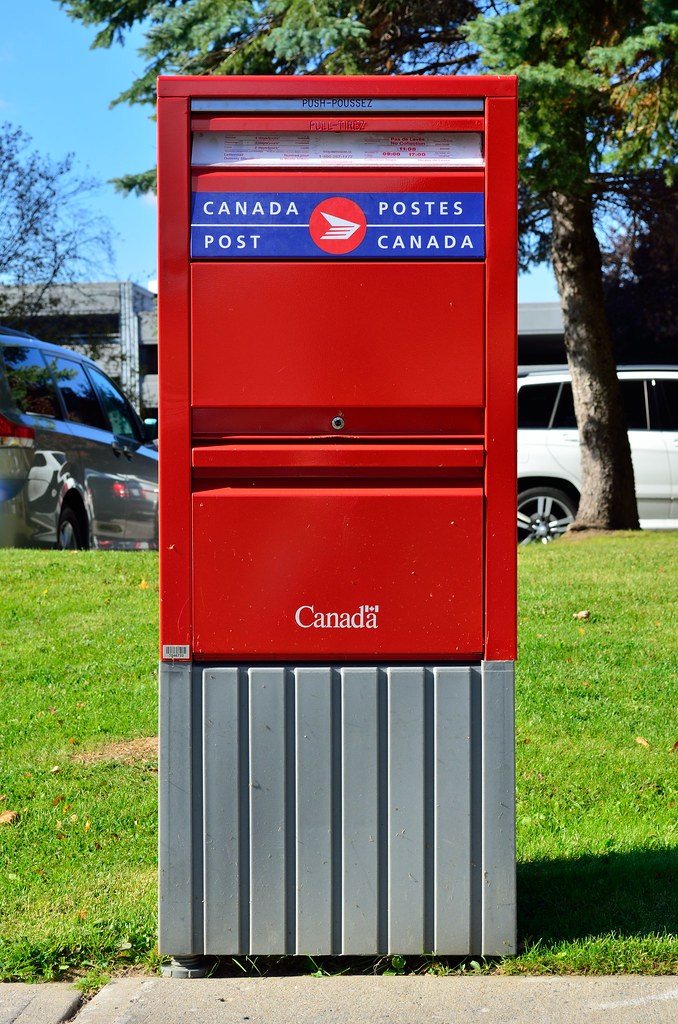 Une boîte aux lettres de Postes Canada sur une pelouse au bord d'un trottoir.