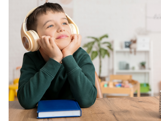 Un enfant souriant légèrement et portant des écouteurs est assis à une table avec un livre dessus.