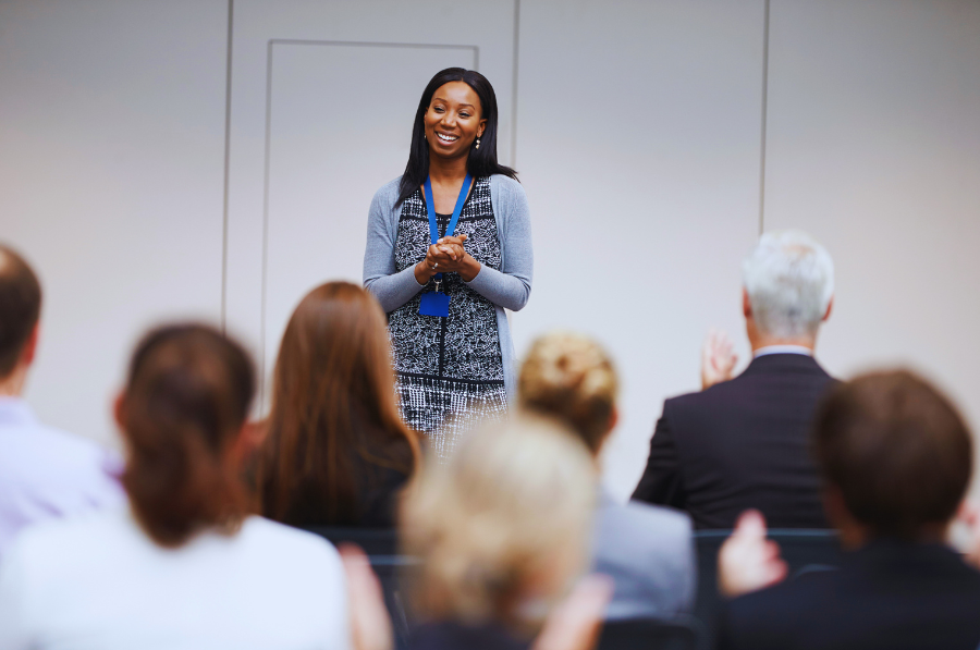 A smiling person faces a seated audience.