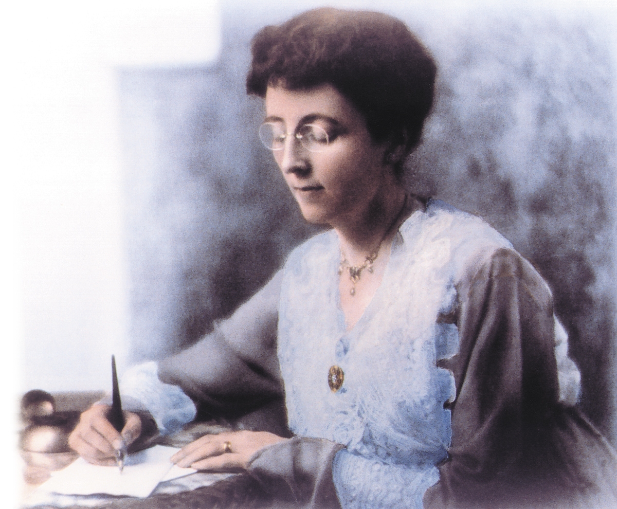 Portrait of Lucy Maud Montgomery seated at a desk and writing with pen and paper.