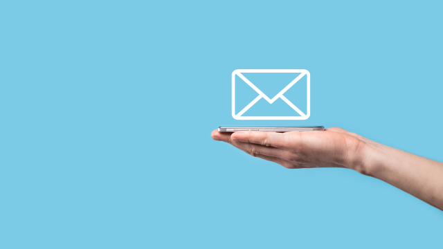Sur un fond bleu clair, une main arrive de la droite du cadre tenant un smartphone dans sa paume. Au-dessus de la paume, le graphique d’une enveloppe semble flotter.
