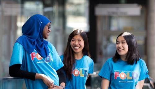 Three young people, one wearing a hijab are talking. They all wear blue FOLD t-shirts.