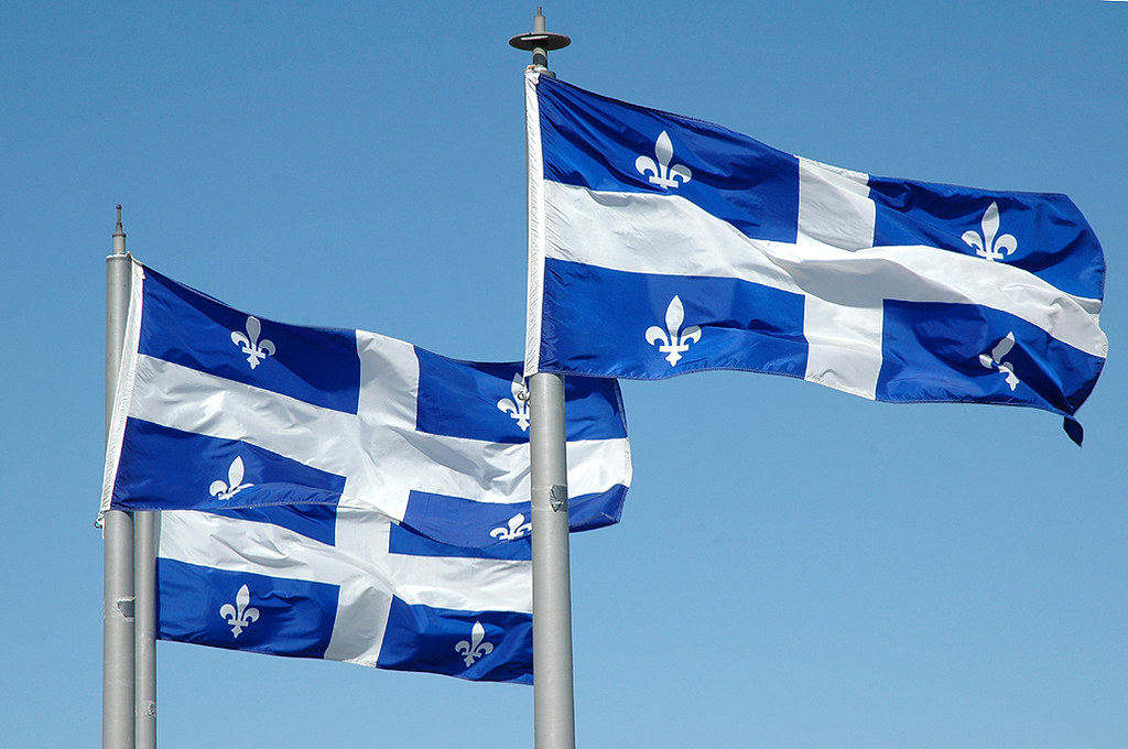 Trois drapeaux du Québec flottent au vent.