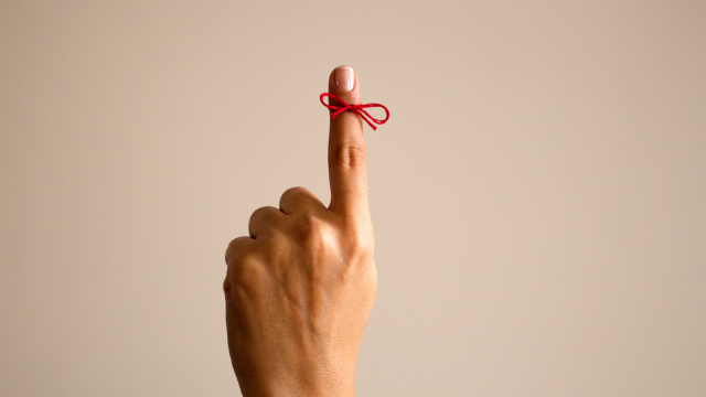 A hand with the index finger pointed up with a red string tied around it.