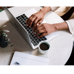 Two hands type on a laptop. Beside the computer is a cup of coffee.
