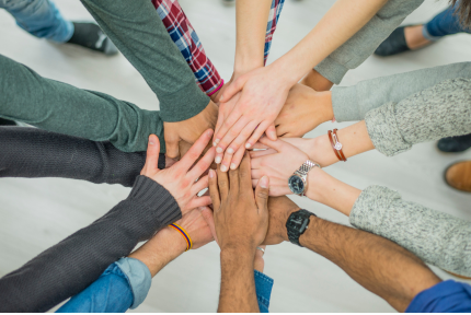 Many hands of different skin tones reach in to touch in the middle of a circle.