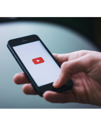 Gros plan d'une main tenant un téléphone avec l'icône de lecture rouge YouTube sur l'écran.