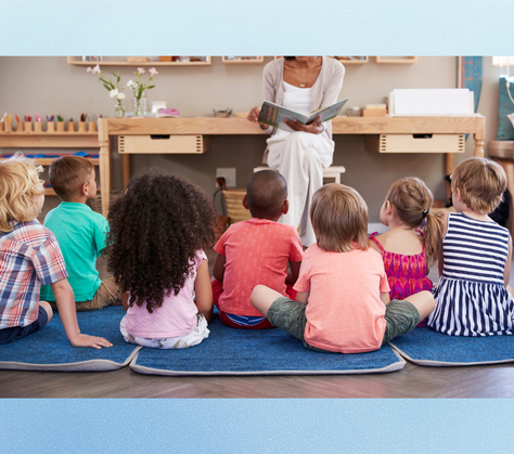 A group of children sitting in front of an adult reading them a story.