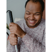 A smiling person holds a white cane.