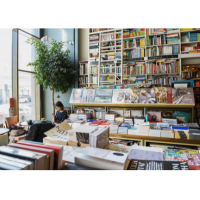 A brightly lit book shop with plants in the window and tables and shelves full of books.
