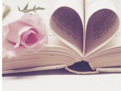 Un livre est ouvert avec une rose rose dessus et deux pages pliées l'une vers l'autre en forme de cœur.