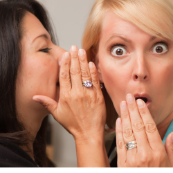 One woman whispers into the ear of a second woman who has a shocked look on her face.