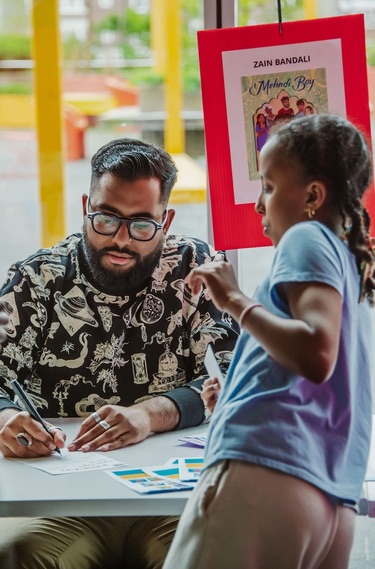 A young person gets a book autographed by an author sitting at a table.