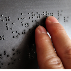 photo en gros plan de deux doigts lisant le braille sur un panneau gris