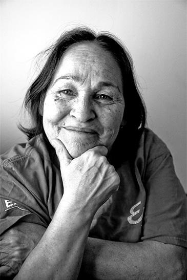 Black and white portrait of Josephine Bacon. A woman with dark hair and a wide smile rests her face on her hand.