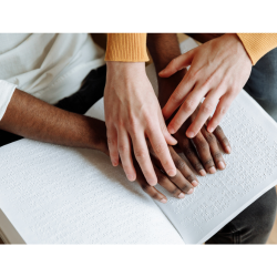 Deux paires de mains lisent ensemble un livre en braille.