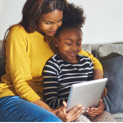 Une femme et un jeune enfant sont assis ensemble sur un canapé et lisent une tablette.