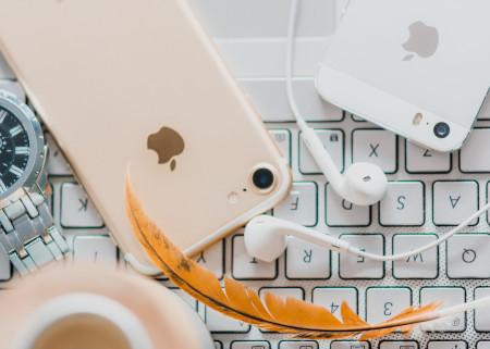 Un iPhone rose, un iPhone blanc, une plume d'or et des écouteurs sur le dessus d'un clavier