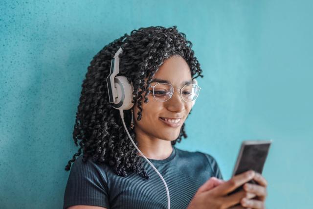 Une jeune femme noire portant des écouteurs blancs et tenant un iPhone qu'elle utilise pour écouter des livres audio