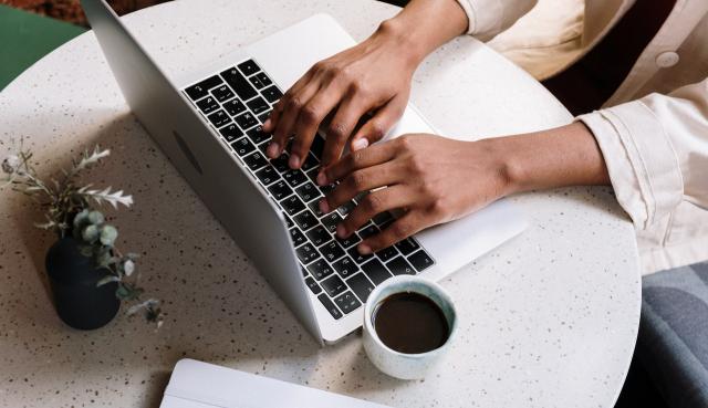 Une femme noire en tapant sur un clavier d'ordinateur portable avec un café et une plante au repos à côté de l'ordinateur