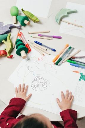 Child sitting at table with paper, crayons and pens