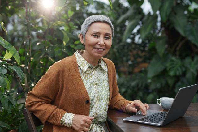 femme âgée en pull marron souriant et utilisant un ordinateur