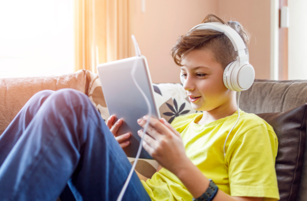  Un enfant portant des écouteurs lit sur une tablette.