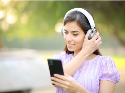 A woman with headphones listens to an audiobook on a phone.