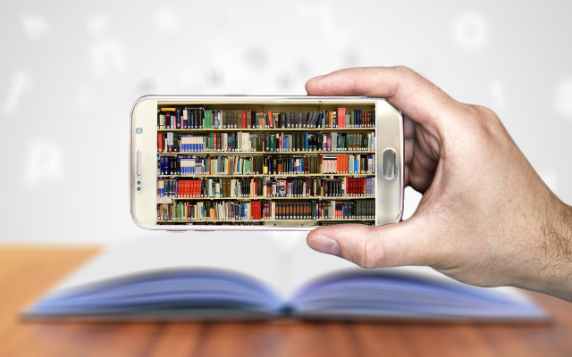 Une main tient un téléphone intelligent dont l'écran affiche une image de bibliothèques ; un livre papier est ouvert à l'arrière-plan